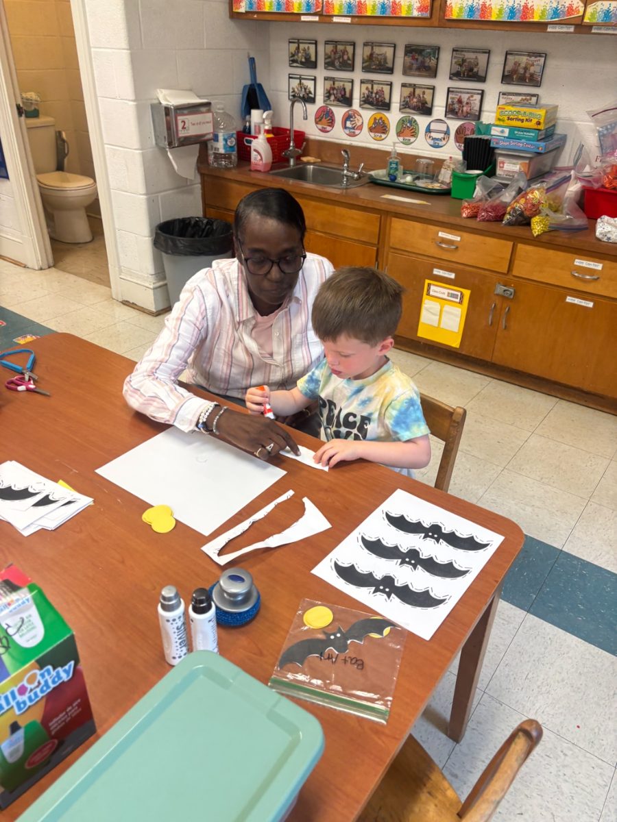 A WEE Center teacher helping a young boy with a craft project at a classroom table